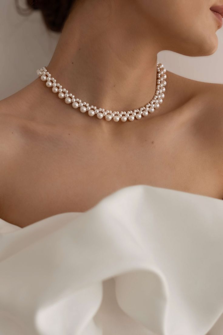 a woman in a white dress wearing a necklace with pearls on the neck and shoulder