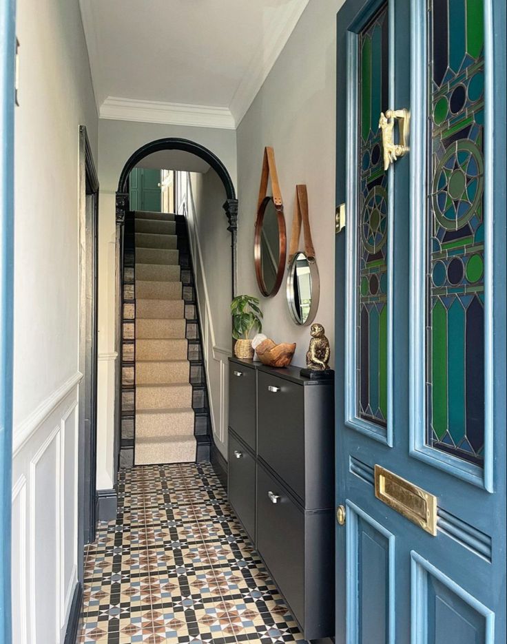 a hallway with blue doors and tiled flooring next to a black cabinet filled with vases