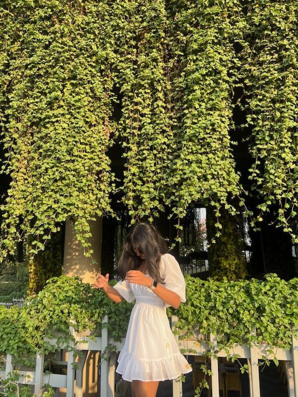 a woman standing in front of a tree covered with green leaves and looking at her cell phone