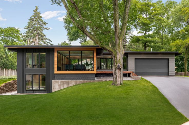 a modern house in the middle of a lush green yard with trees and grass on both sides