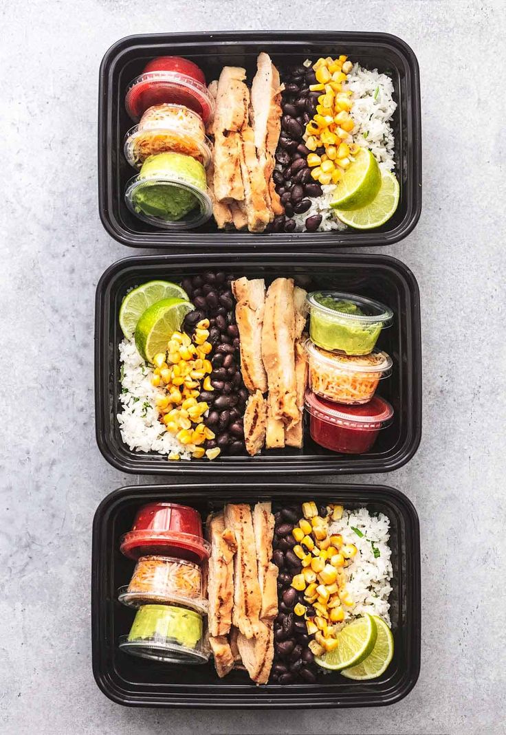 three black trays filled with different types of food on top of a white table