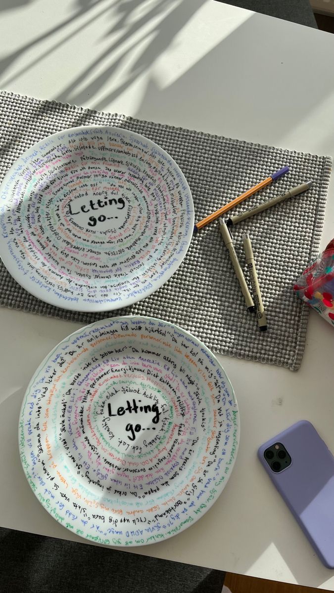 two white plates with writing on them next to a cell phone and pencils sitting on a table