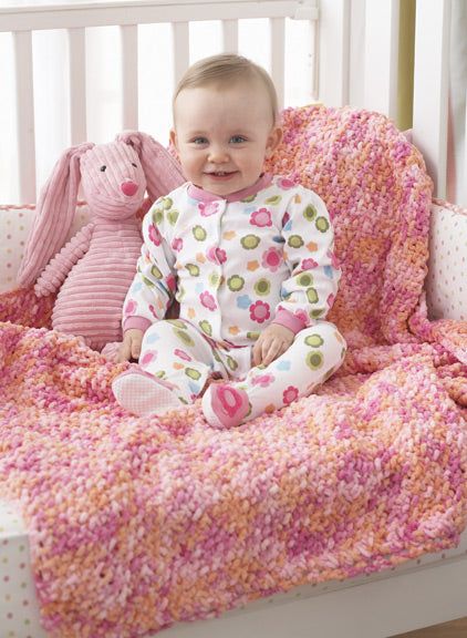 a baby is sitting in a crib with a pink blanket and stuffed animals on the bed