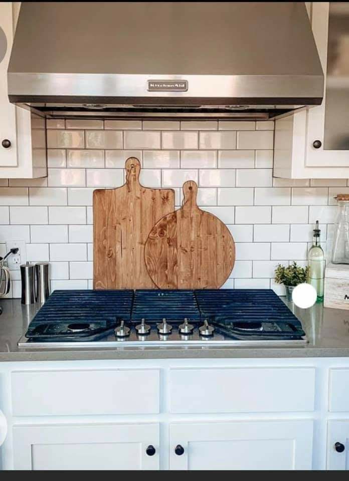 a cutting board sitting on top of a stove in a kitchen next to white cabinets