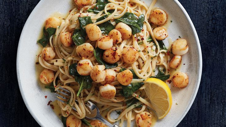 pasta with scallops, spinach and lemon wedges on a white plate