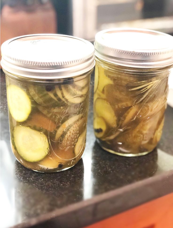 two jars filled with pickles sitting on top of a counter