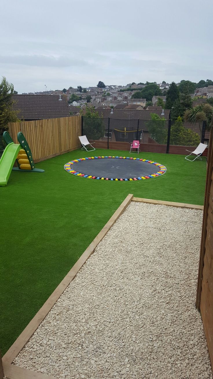 a backyard with artificial grass and a trampoline in the back ground, next to a play area