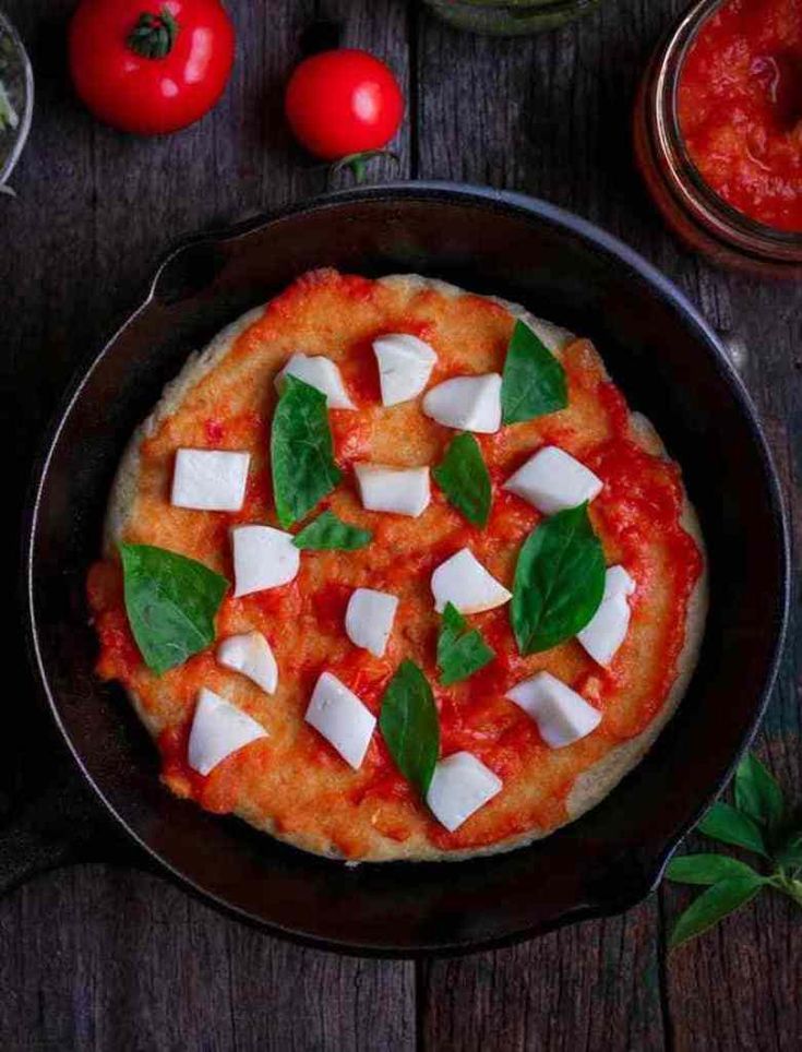 a pizza in a pan topped with mozzarella, basil and cheese on a wooden table