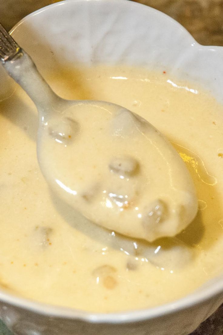 a white bowl filled with cheese sauce and a spoon on top of the soup in it