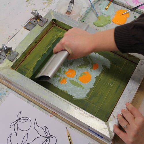 a person is using a brush to paint an image on paper with oranges and green leaves