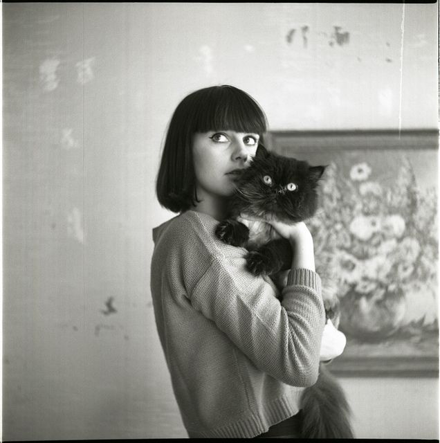 a woman holding a black cat in her right hand and looking up at the camera