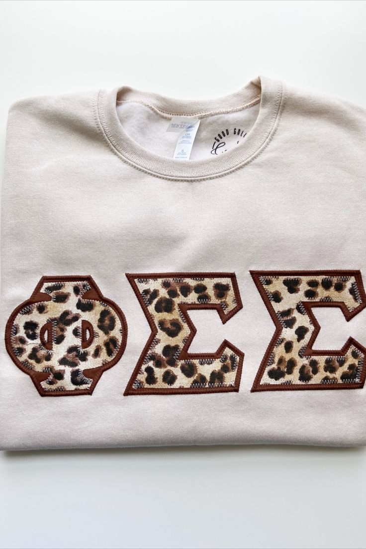 a white t - shirt with leopard print on the front and two letters that spell phi