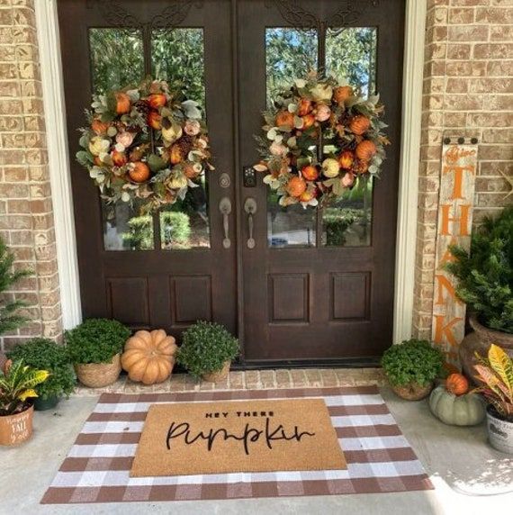 front door decorated with wreaths and pumpkins for the fall season, next to a welcome mat that says happy thanksgiving