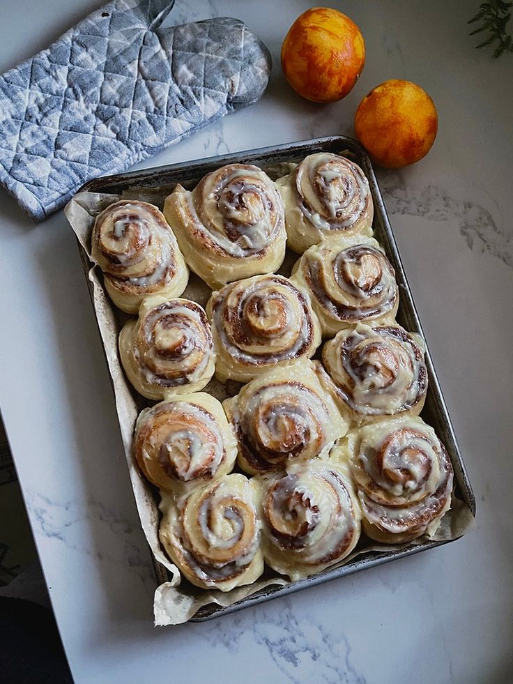 a pan filled with cinnamon rolls on top of a counter next to an orange peel