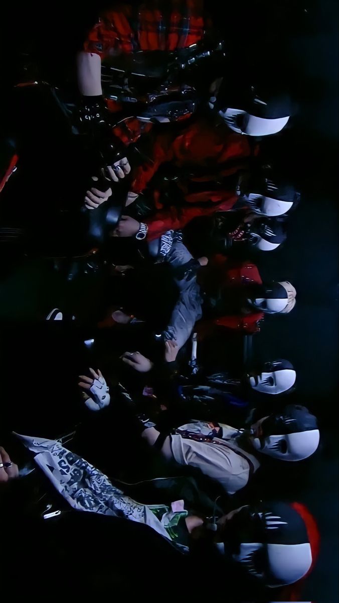 a group of people sitting next to each other in front of a black wall with helmets on it