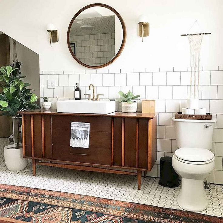 a white toilet sitting next to a wooden sink vanity in a bathroom under a round mirror