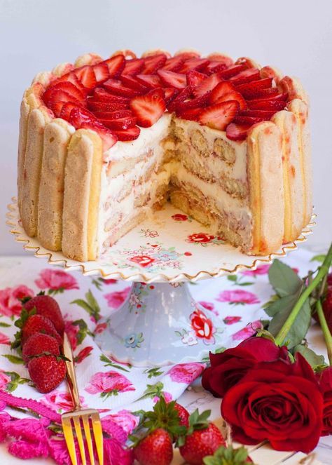 a cake with strawberries on top is cut in half and sits on a floral tablecloth