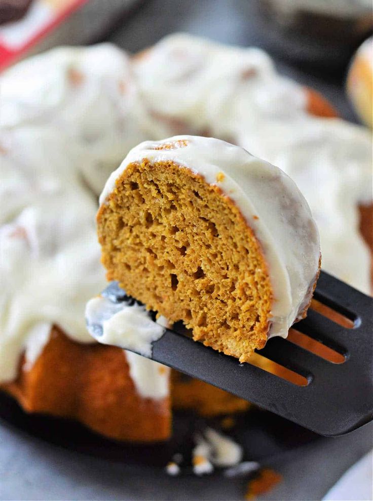 a piece of cake being held up by a fork with icing on it and some muffins in the background