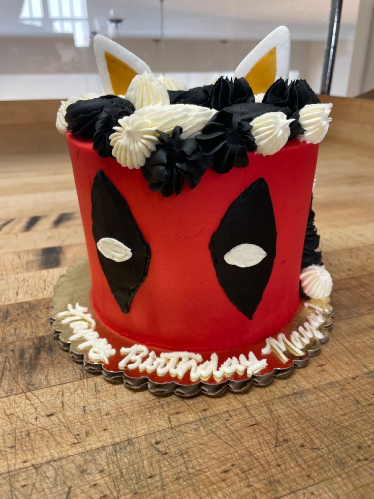 a red cake with white frosting and black flowers on it's face is sitting on a wooden table