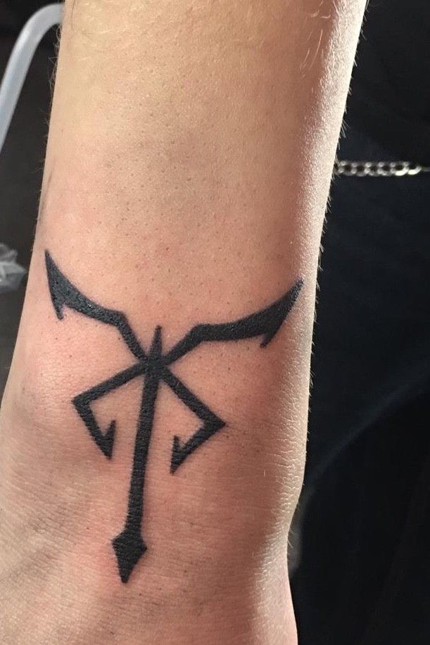 a tattoo on the wrist of a person with an arrow and cross in black ink