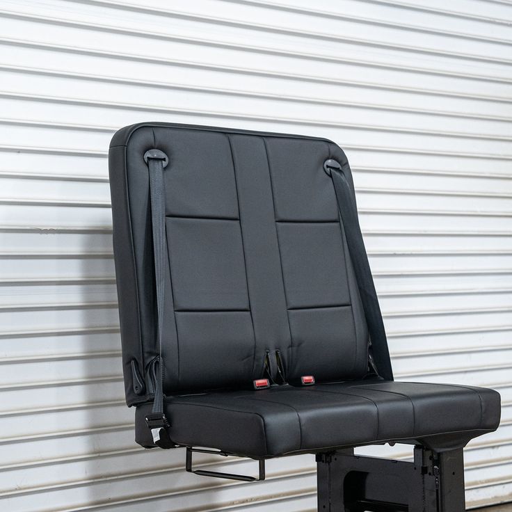 a black chair sitting on top of a metal stand in front of a garage door