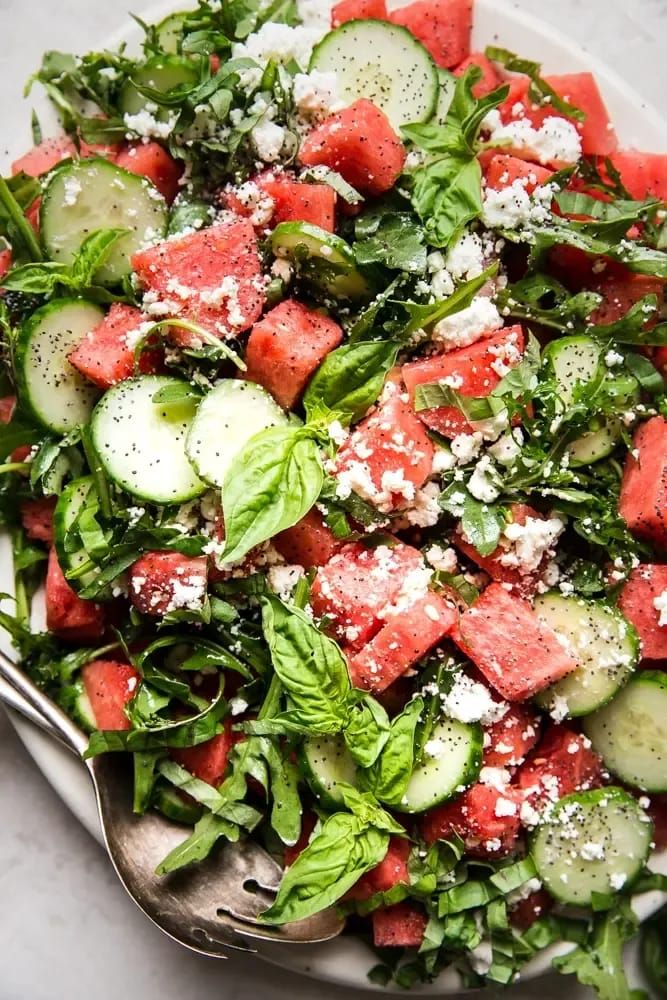 watermelon and cucumber salad on a white plate with silver spoons