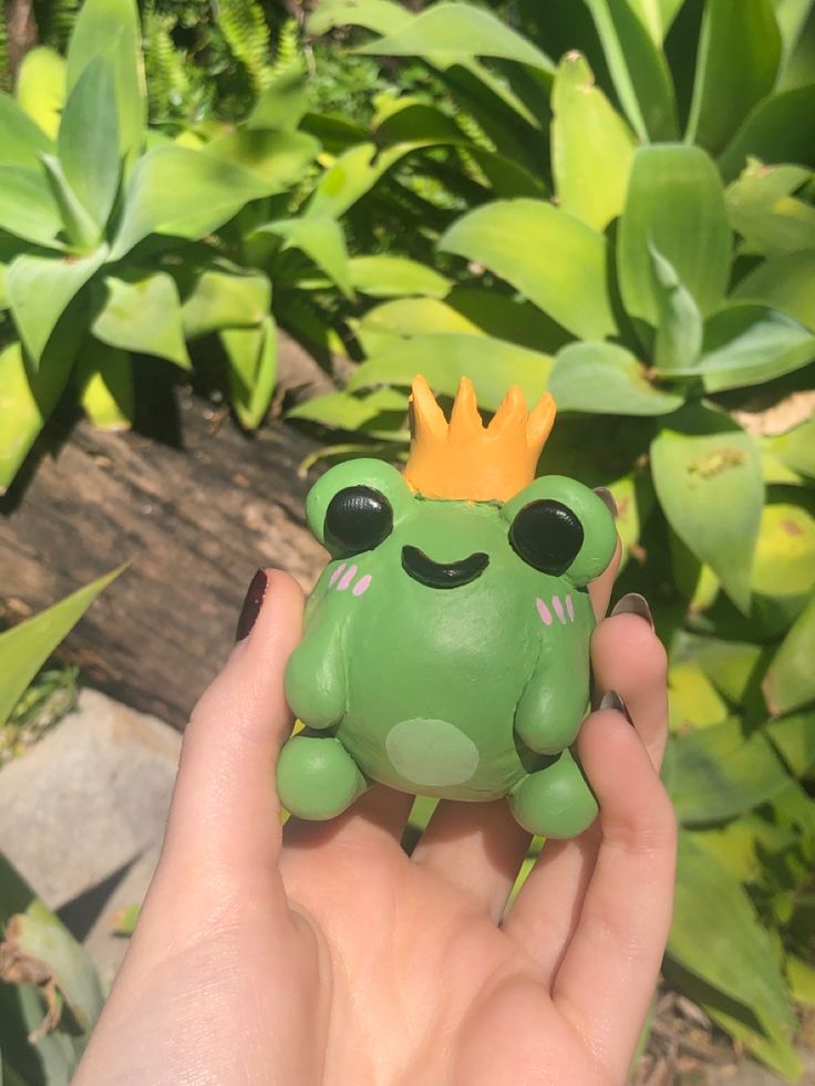 a hand holding a small green frog with a crown on it's head