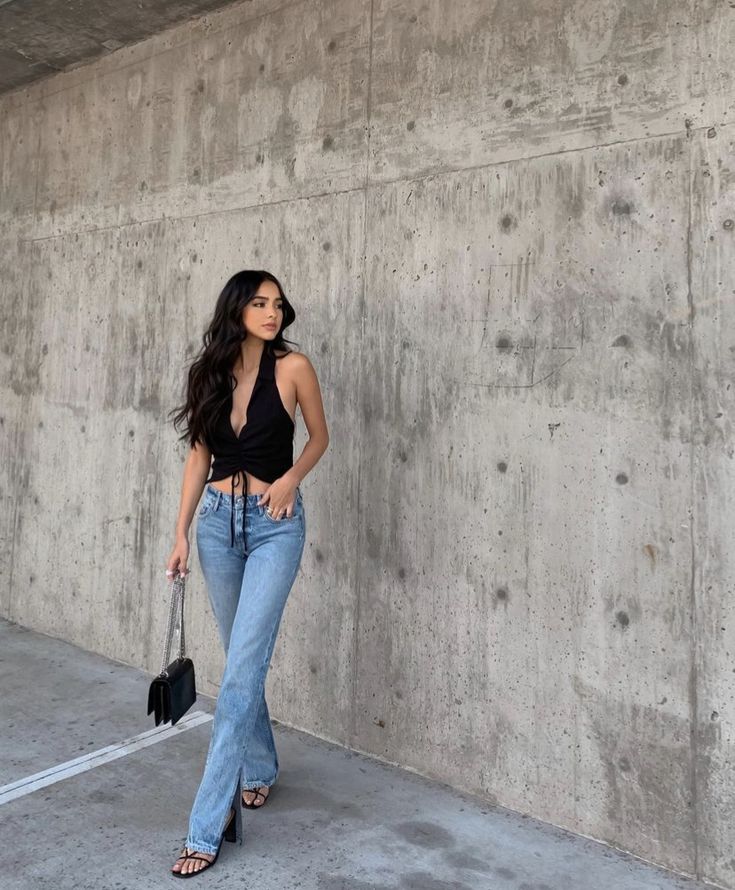 a woman standing in front of a concrete wall with her hand on her hip and looking at the camera