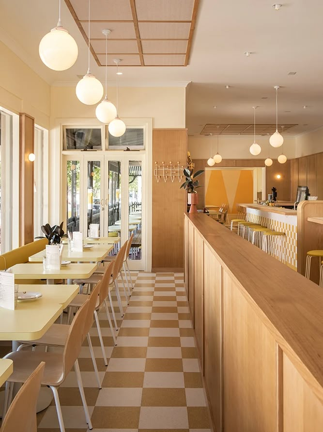 an empty restaurant with yellow and white checkered flooring on the walls, along with wooden tables and chairs