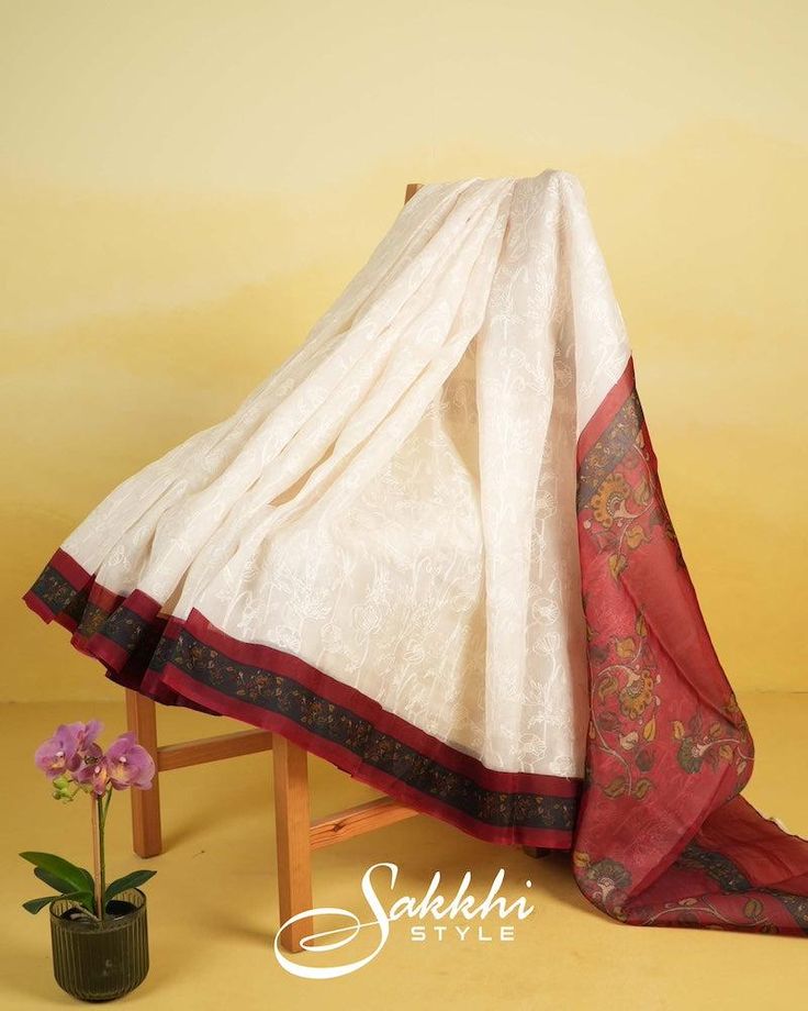 The embroidered white saree, adorned with a vibrant red border, paints a picture of timeless elegance. Each delicate stitch tells a story of tradition and grace, while the printed motifs add a touch of modern allure. The stitched blouse, with its intricate design, harmonizes beautifully with the saree's rich tapestry. Wrapped in this ensemble, she exudes confidence and charm, embodying a blend of tradition and contemporary flair that captivates with every graceful step. * Organza silk saree for special occasions. * Crafted from the premium quality fabric. * Supplied with a readymade blouse. * The blouse comes with an added allowance, and it can be altered to a standard size of 34"-42" on request. * Dry clean only to maintain colour and quality. Traditional White Chanderi Pre-draped Saree, Traditional White Pre-draped Saree With Embroidered Border, Traditional Pre-draped Cotton Silk Saree With Embroidered Border, Red Cotton Silk Traditional Wear With Embroidered Border, Traditional Red Cotton Silk Wear With Embroidered Border, Red Traditional Wear With Embroidered Border In Cotton Silk, White Slub Silk Dupatta With Embroidered Border, White Silk Traditional Wear With Embroidered Border, Cotton Silk Saree With Embroidered Border