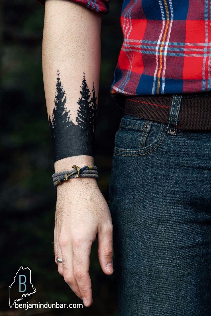 a person with a forest tattoo on their arm holding onto the wrist and wearing a bracelet