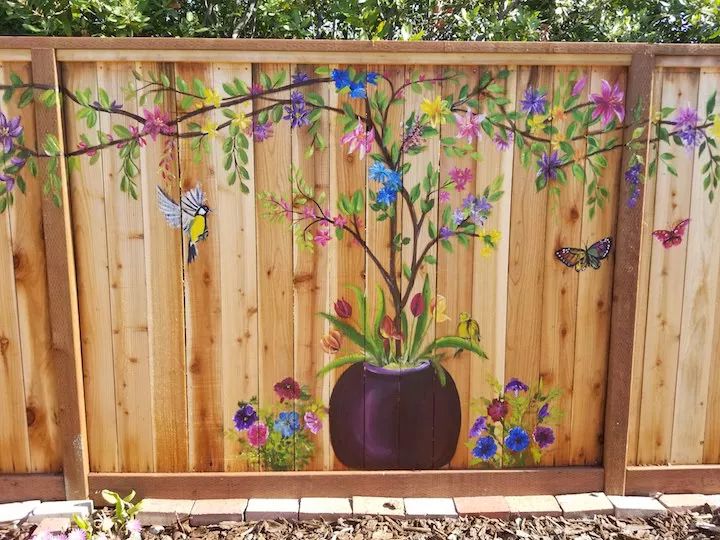 a wooden fence with flowers painted on it and butterflies flying over the plant in the vase