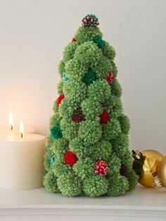 a green christmas tree sitting next to a lit candle on top of a white table