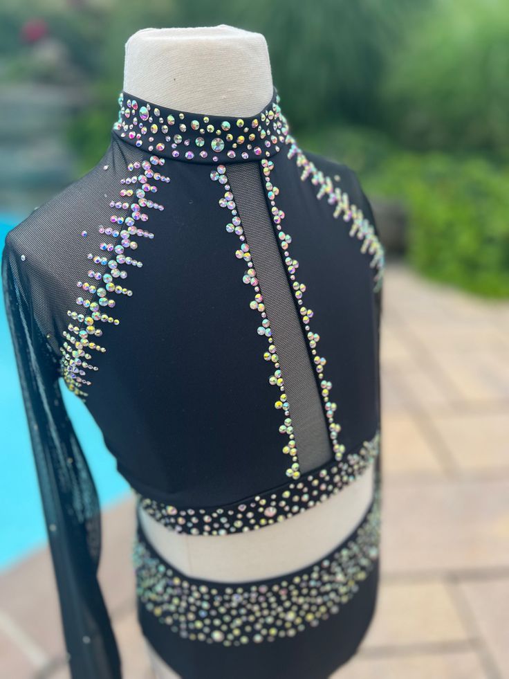 the back of a black and white dress with beads on it, next to a swimming pool