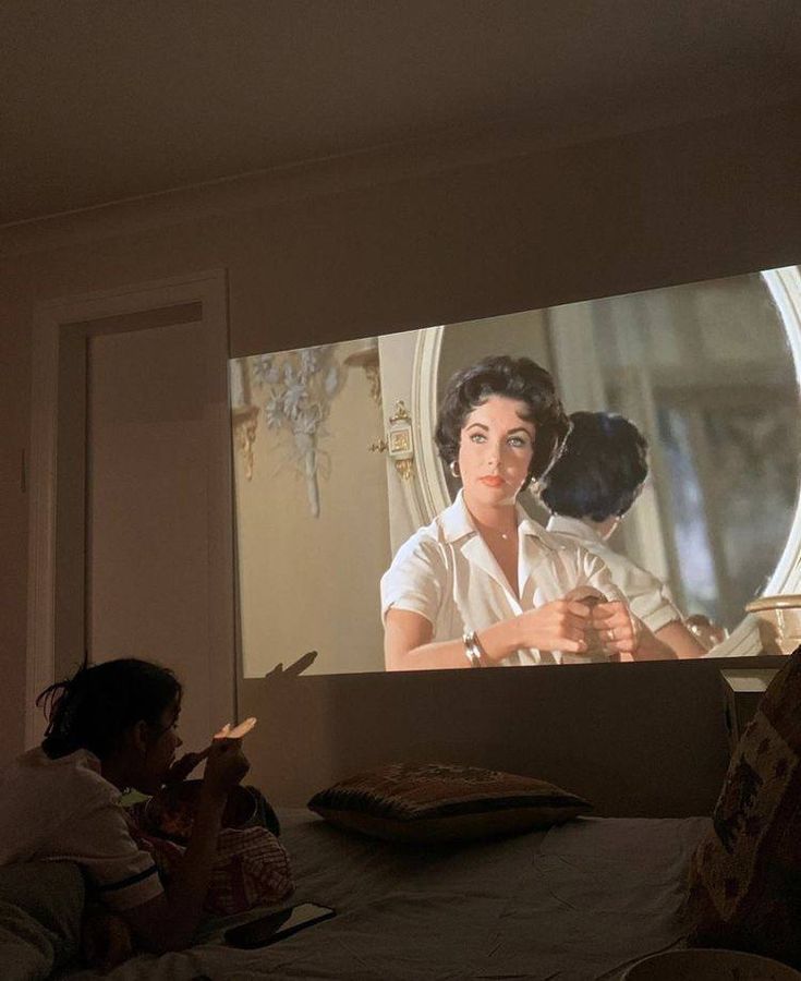 two people sitting on a bed in front of a large screen with an image of a woman and child