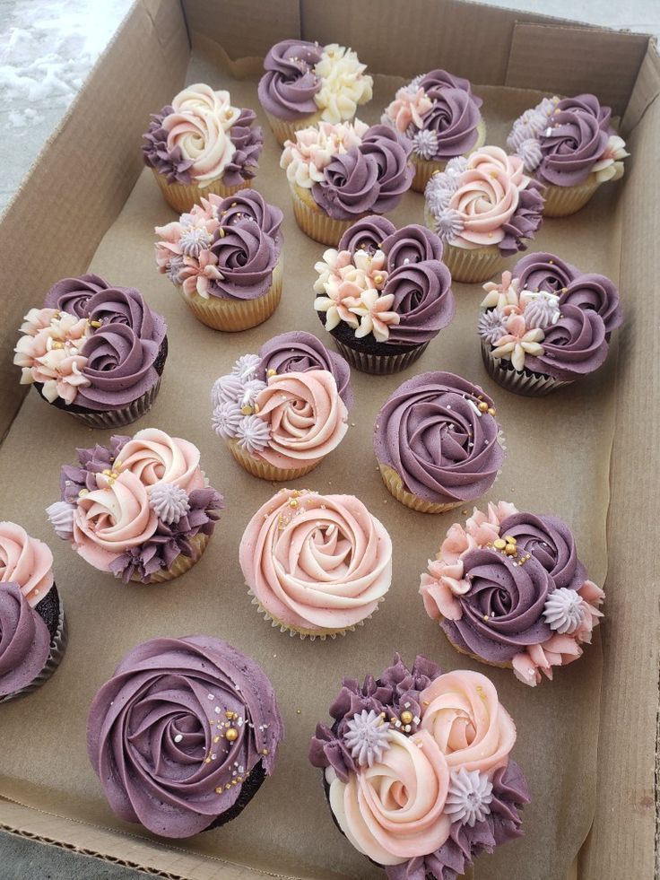 a box filled with lots of cupcakes covered in purple frosting and flowers