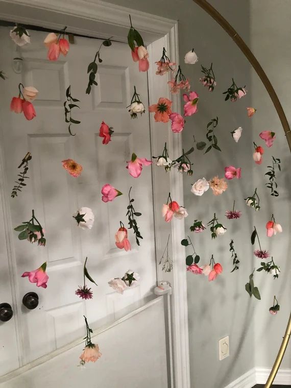 a white door with pink and red flowers hanging from it's side, in front of a mirror