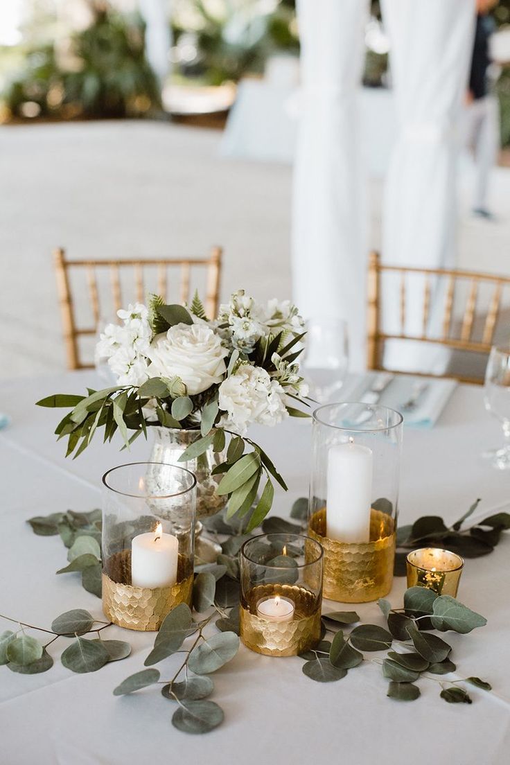 white flowers and greenery are arranged on a table with gold vases for centerpieces