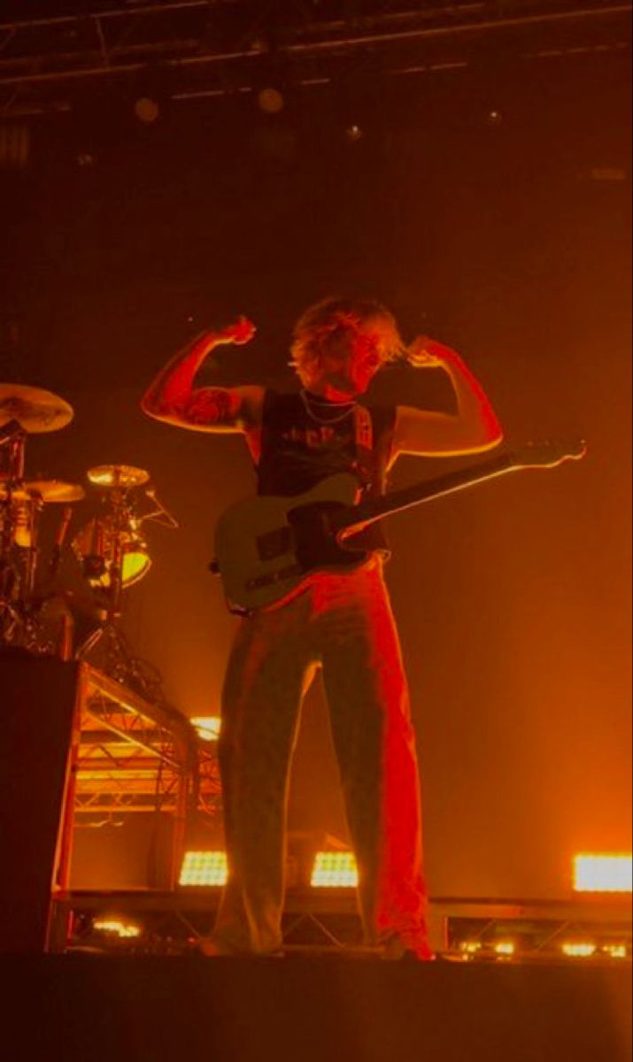 a man standing on top of a stage with his guitar in hand and another person behind him