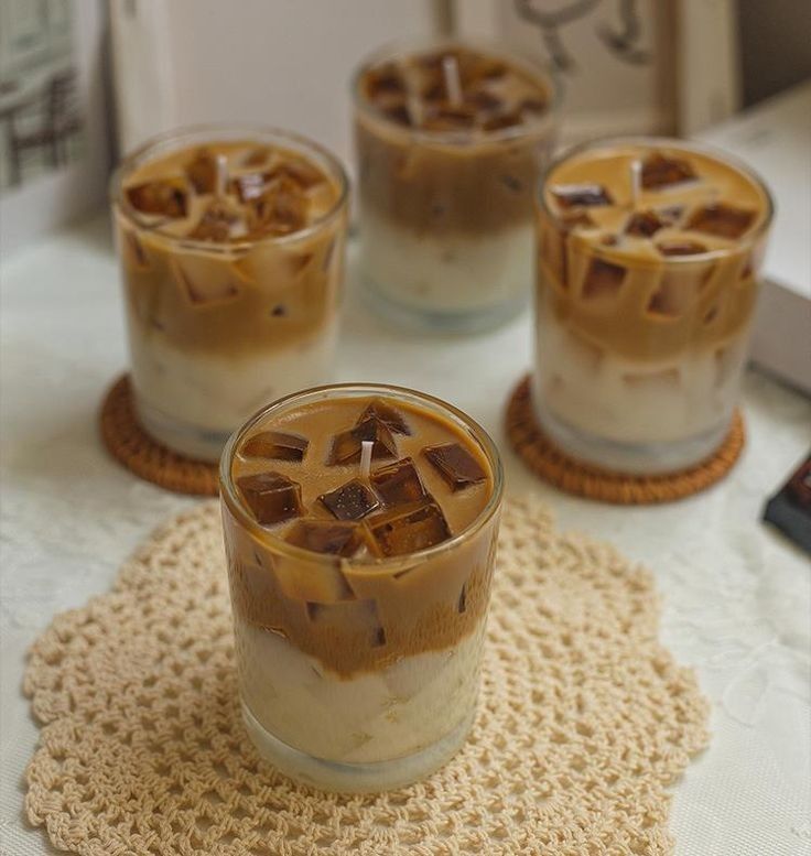 three glasses filled with ice cream on top of a doily next to a book