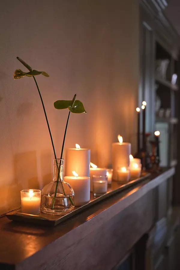 candles are arranged on a shelf with flowers in vases