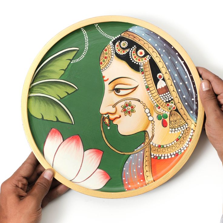 two hands holding a decorative plate with a painting on the front and back of it