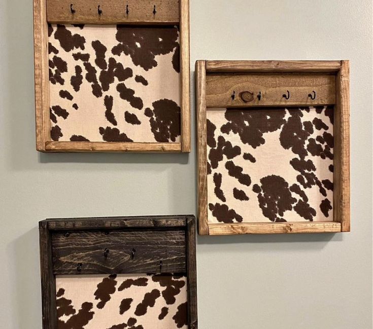 three wooden frames with brown and white cow prints on them, hanging on the wall