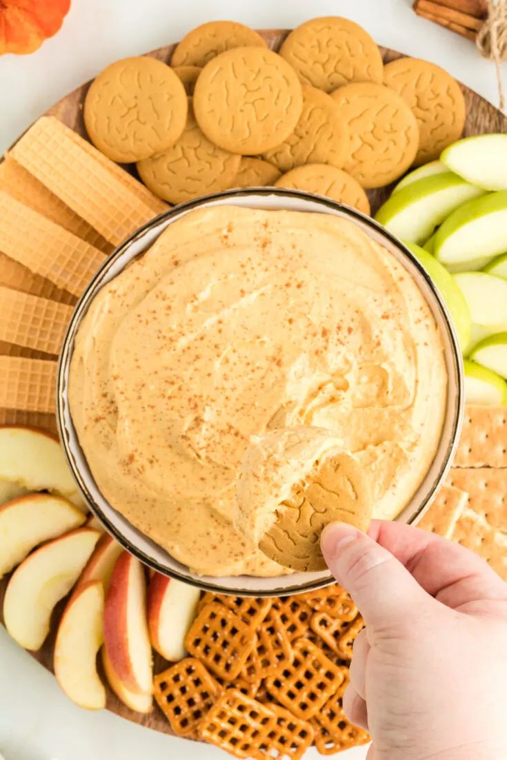 a person dipping peanut butter into an apple slice and cracker on a platter