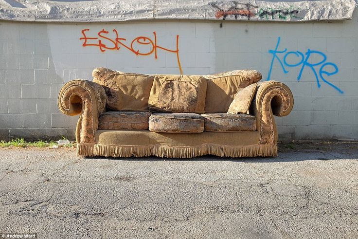 an old couch sitting in front of a wall with graffitti on it's side