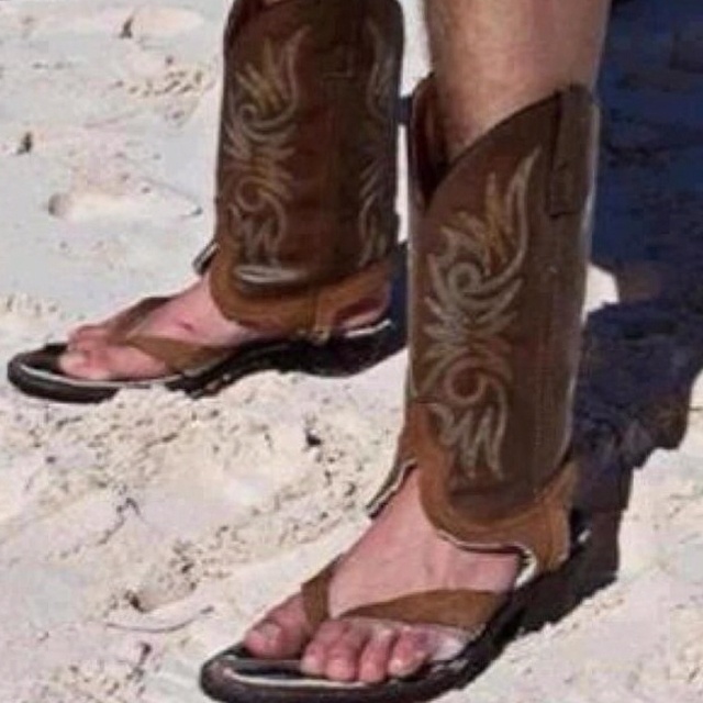 a person wearing cowboy boots standing in the sand