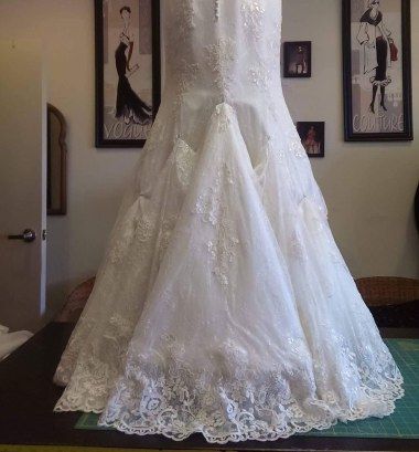 a wedding dress is displayed in front of two framed pictures on the wall behind it