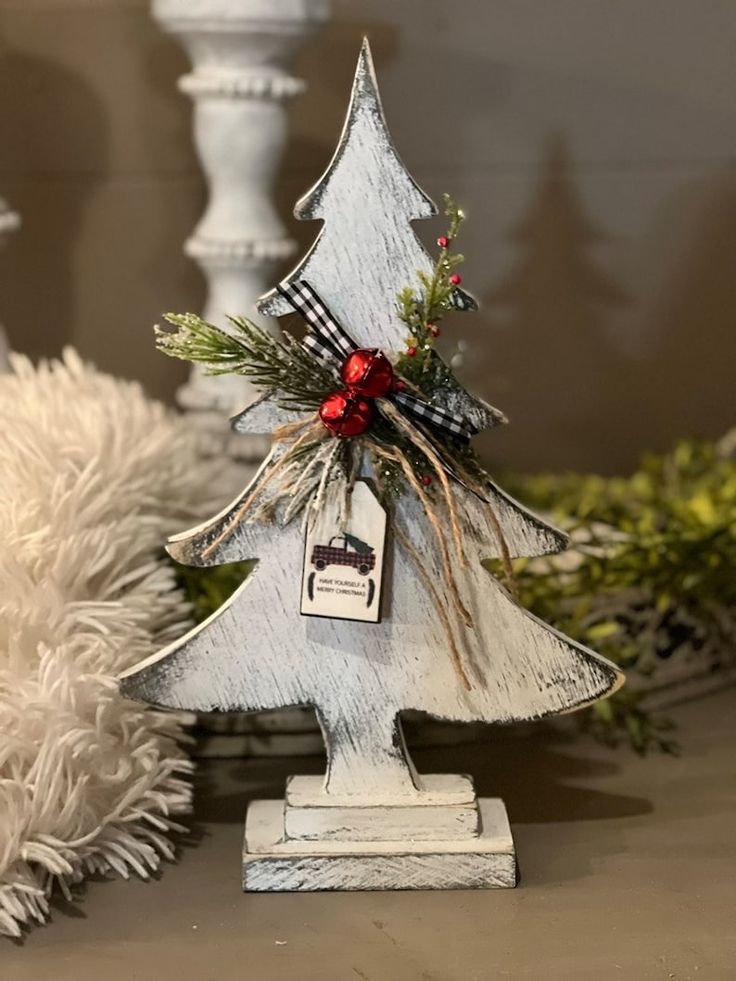 a small wooden christmas tree sitting on top of a table next to white candlesticks