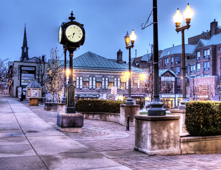 a clock on a pole in the middle of a street with buildings and lights around it