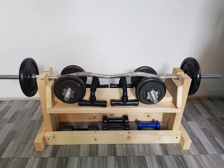 a gym bench with two dumbs and one barbell on it in front of a white wall